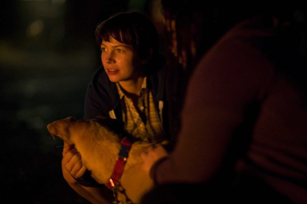 Wendy (Michelle Williams) pats her dog Lucy by the fireside at night in Wendy and Lucy, directed by Kelly Reichardt.