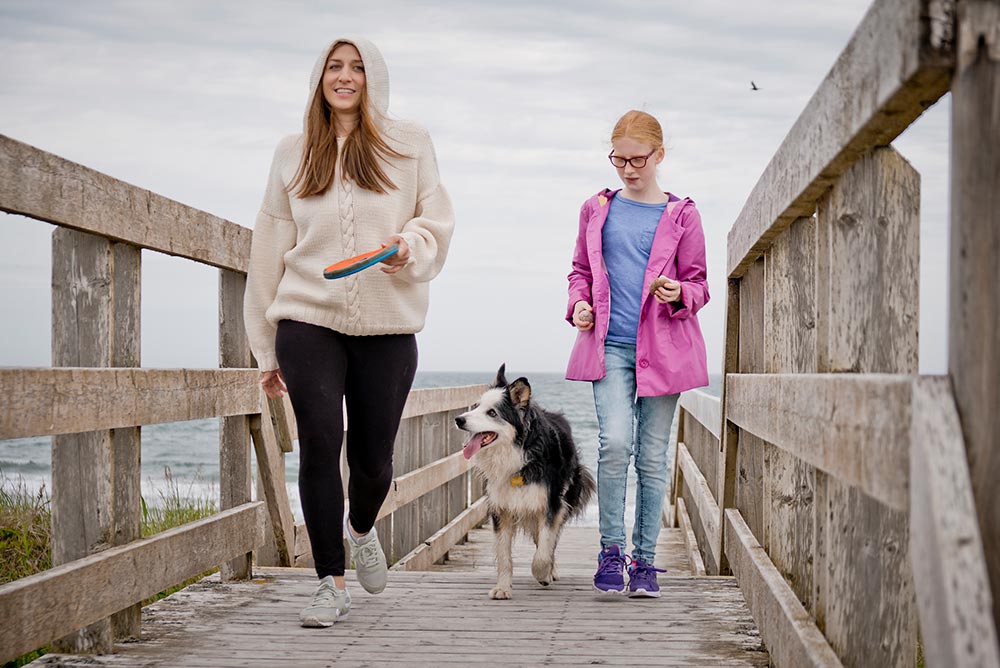 A still from Spinster, featuring Chelsea Peretti as Gaby with her character's dog and young niece, walking by the seaside.