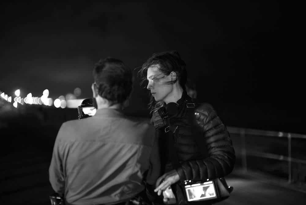 A black and white image of Eva Riley speaking to cinematographer Steven Cameron Ferguson on the set of Perfect 10. They are standing by the sea.