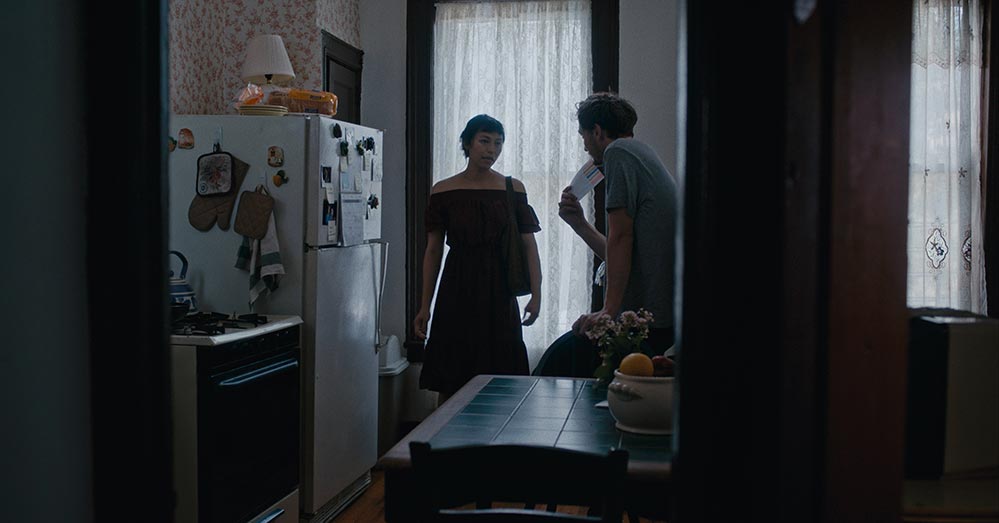 Isabel Sandoval as Olivia and Eamon Farren as Alex in Lingua Franca. The two characters are speaking in a kitchen, shot through a doorway.