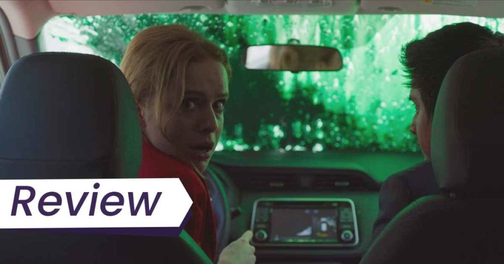 A still from New Order in which a woman in a car looks, panicked, behind her shoulder. The car's windscreen is covered in green paint.