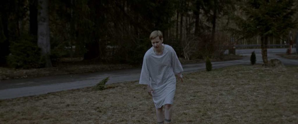 Marlene (Sandra Hüller), wearing a hospital gown, walks by the forest in the film Sleep, directed by Michael Venus, screening at Fantasia Festival.