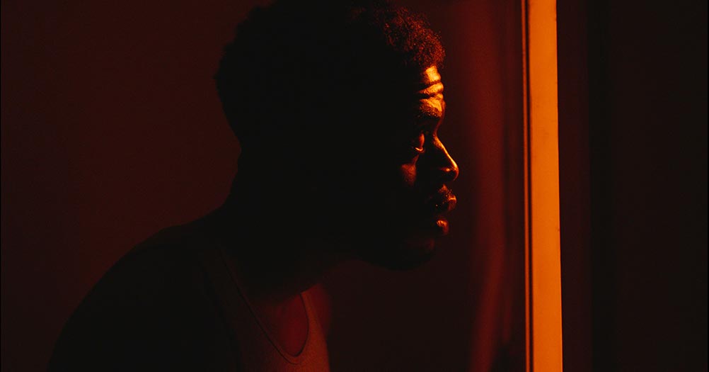 Obinna Nwachukwu as Jay in Residue, looking toward screen right in a darkened room.
