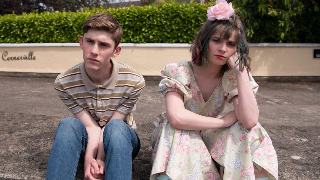 Still of Fionn O'Shea and Lola Petticrew in Dating Amber, screening at InsideOut 2020. They're both sitting on a curb looking despondent.