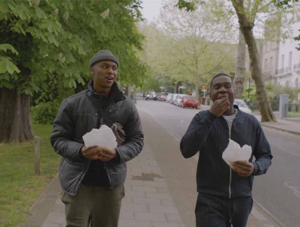 A still off two men eating on the street from Mandem, one of the best short films at LFF 2020.
