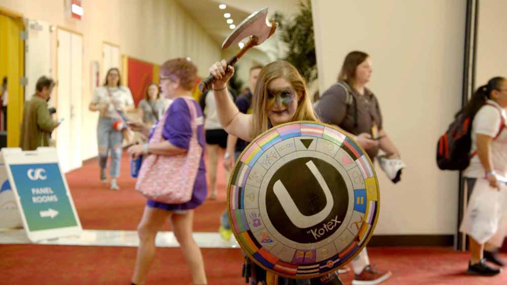 A man holds up a shield and axe at a fan convention.