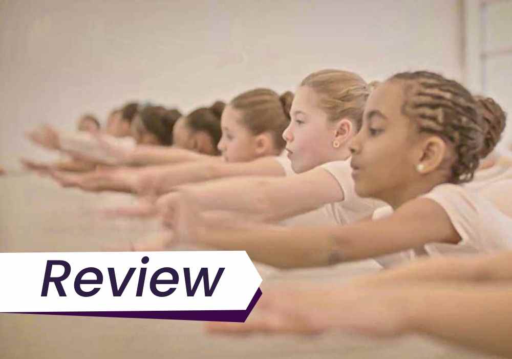 A row of children stretch their arms out in unison, in a dance class. The image is accompanied by the text, 'Review'.