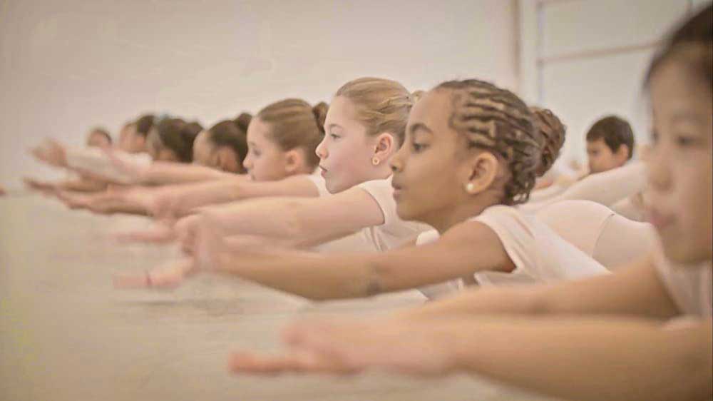 A row of children stretch their arms out in unison, in a dance class.