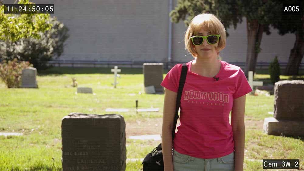 A still from I Blame Society in which Gillian Horvat looks into the camera wearing sunglasses and a pink shirt.