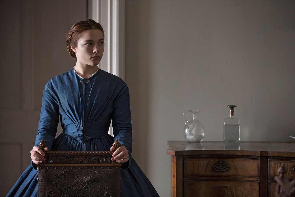 Katherine in Lady Macbeth looks off screen, clutching the back of a chair, her face a blank mask.