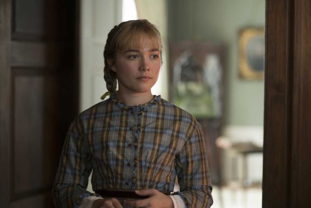 Florence Pugh as younger Amy in Little Women looks toward the distance, playing with her hands.