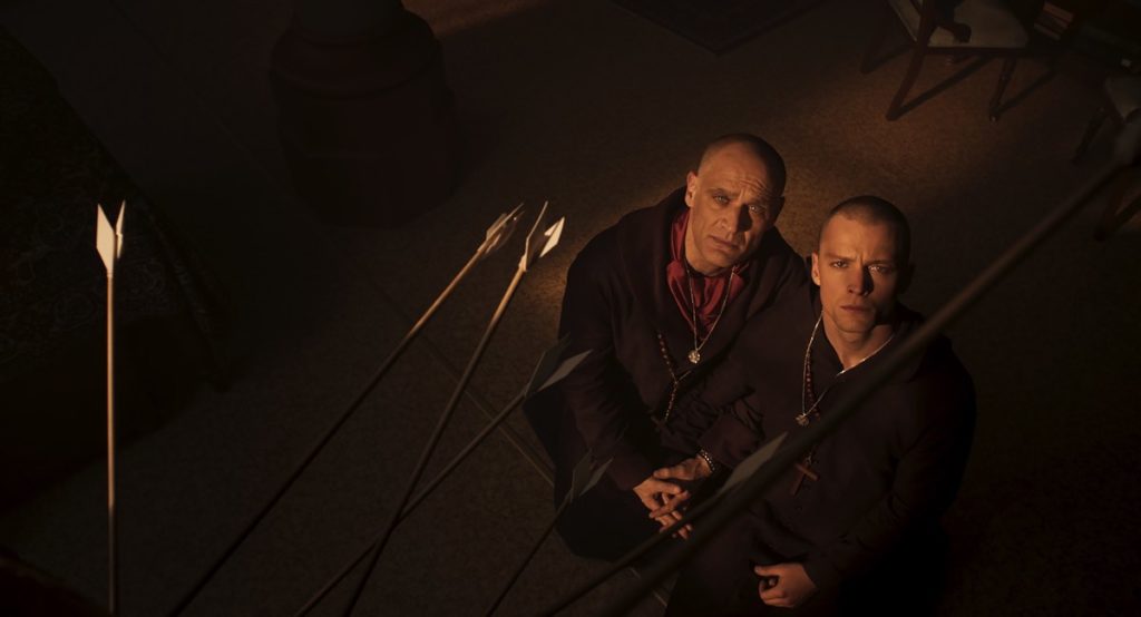 Andreas Apergis (left) stars as Father Andrew an Félix-Antoine Duval (right) stars as Daniel in Bruce LaBruce's Saint-Narcisse. Here, they are wearing their monks' robes in church, staring up at a painting. 