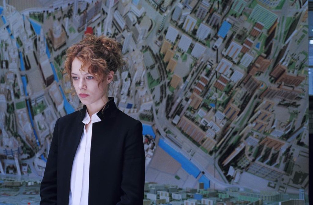 Paul Beer stars in Undine as Undine, standing in front of a map of Berlin, courtesy of Festival du Nouveau Cinema