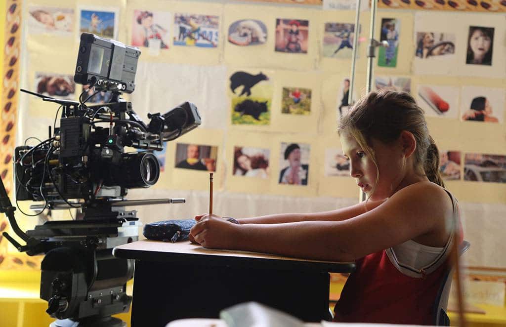 Lake Delisle in front of the camera in a classroom on the set of Rustic Oracle