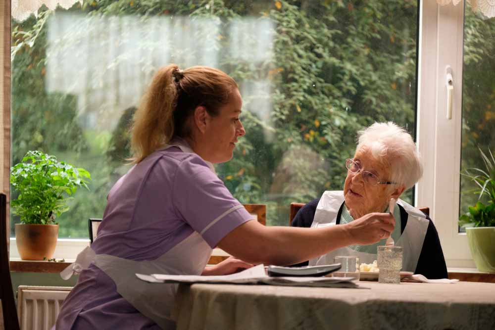 Debbie Honeywood wears an apron and helps an elderly woman eat her meal in Sorry We Missed You.