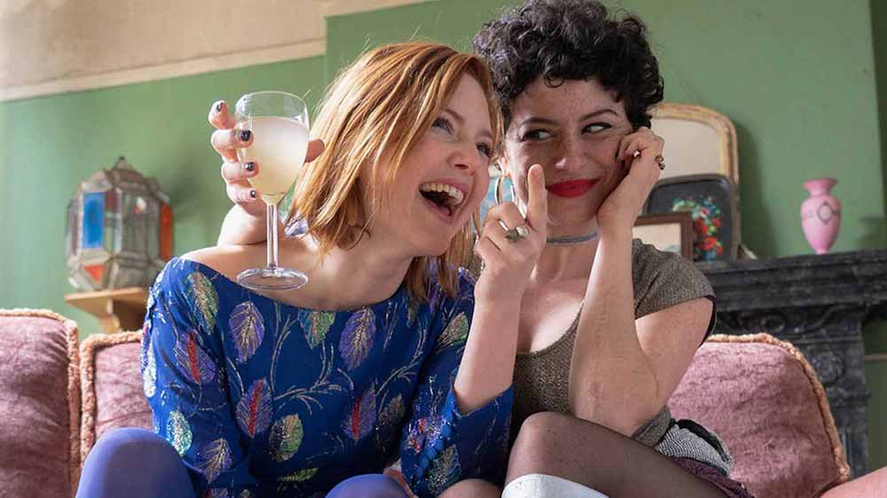 Holliday Grainger and Alia Shawkat laugh together holding glasses of white wine in Animals.