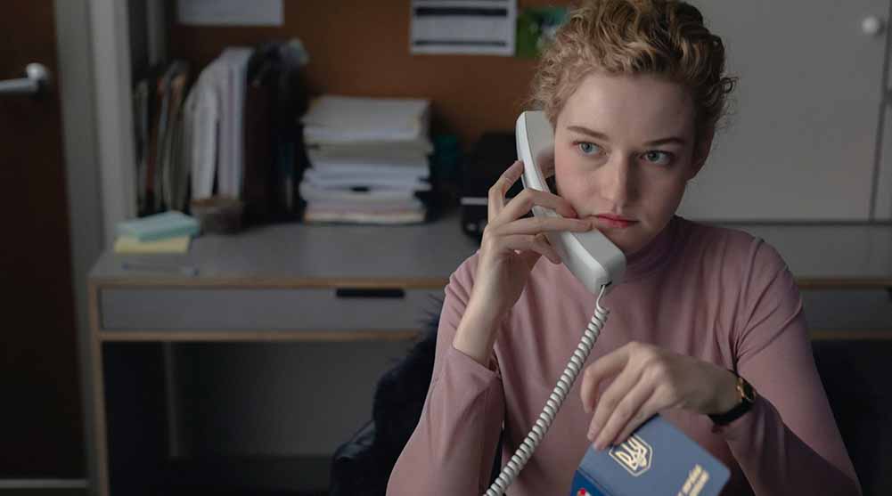 Julia Garner sits at an office table, an office phone to her ear, in The Assistant.