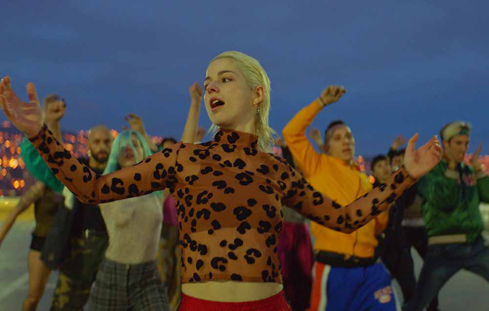 Mariana Di Girólamo dances at the front of a group against a dark blue sky in Ema.