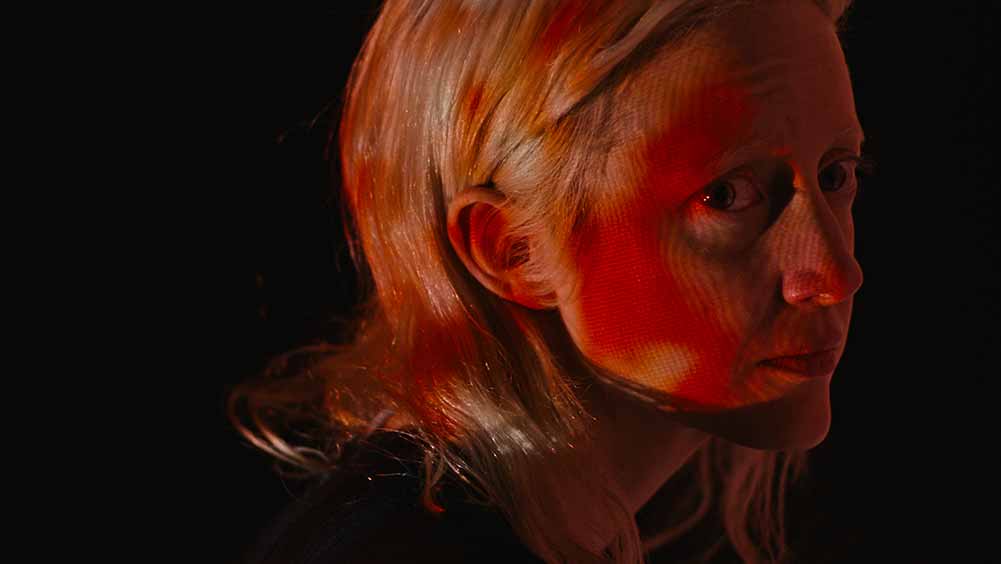 A closeup of Andrea Riseborough as Vos, her face bathed in patchy red light.