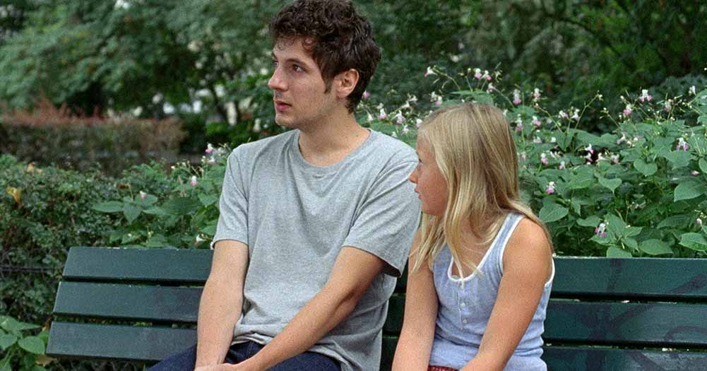 A man in his twenties holds back tears on a park bench, sitting next to his young niece, in Amanda.