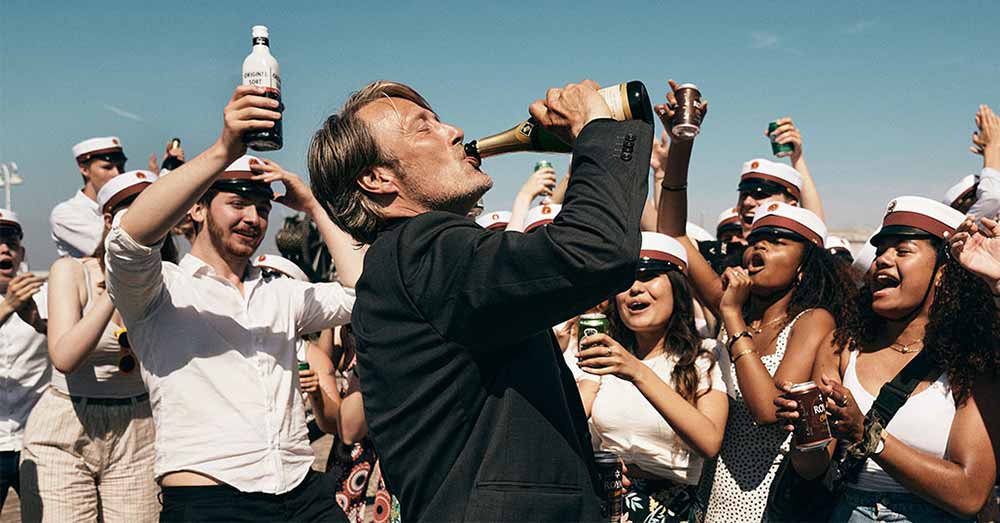 Mads Mikkelsen chugs a bottle of champagne in front of a crowd of cheering high school graduates in Another Round