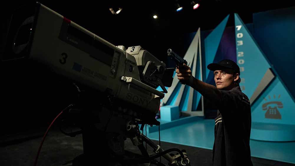A still from Prime Time, in which Bartosz Bielena holds a gun up to a TV camera.