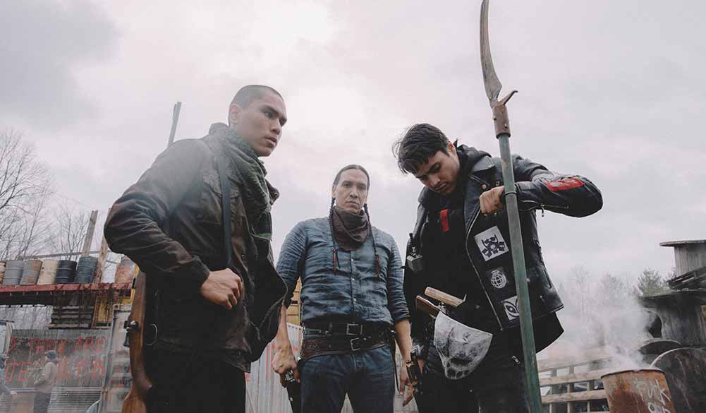 Three Indigenous men stand clustered together, armed with weapons, in Blood Quantum.