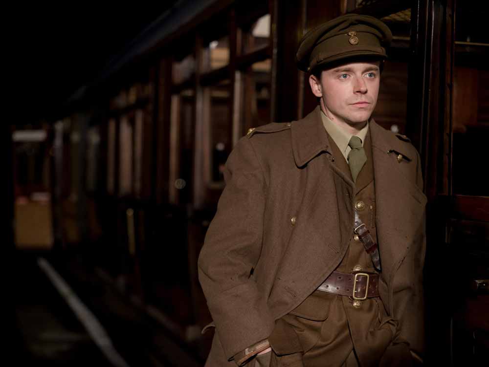 A man in soldier's uniform stands next to a train in Benediction, one of our most anticipated films of 2021.