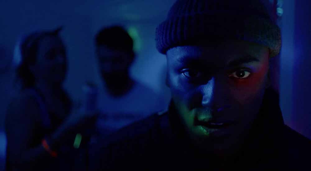 A closeup of a man bathed in blue light in Mandem, an LSFF 2021 title.