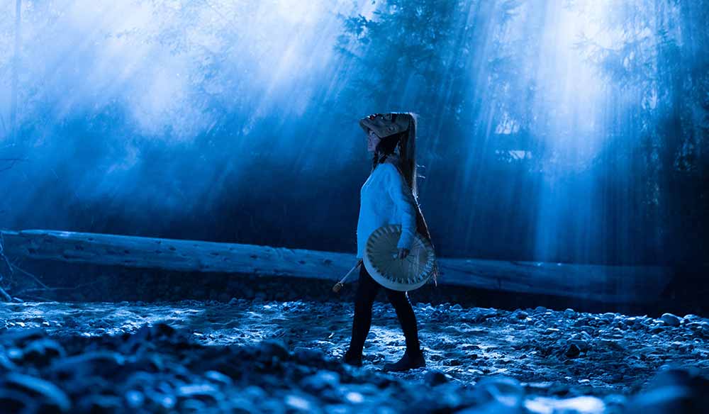 A woman in wooden armour walks through a mesmerising blue haze in Monkey Beach. Still from Monkey Beach, one of the essential Indigenous films from the territories known as Canada.