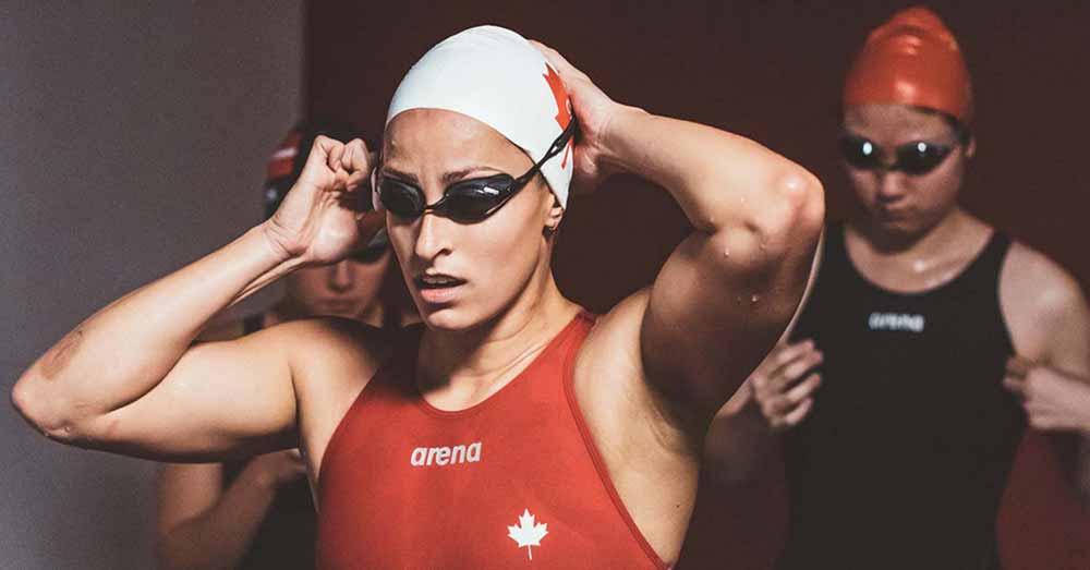 A swimmer puts on her goggles, preparing for a race, in a team Canada swimsuit, in Nadia Butterfly.