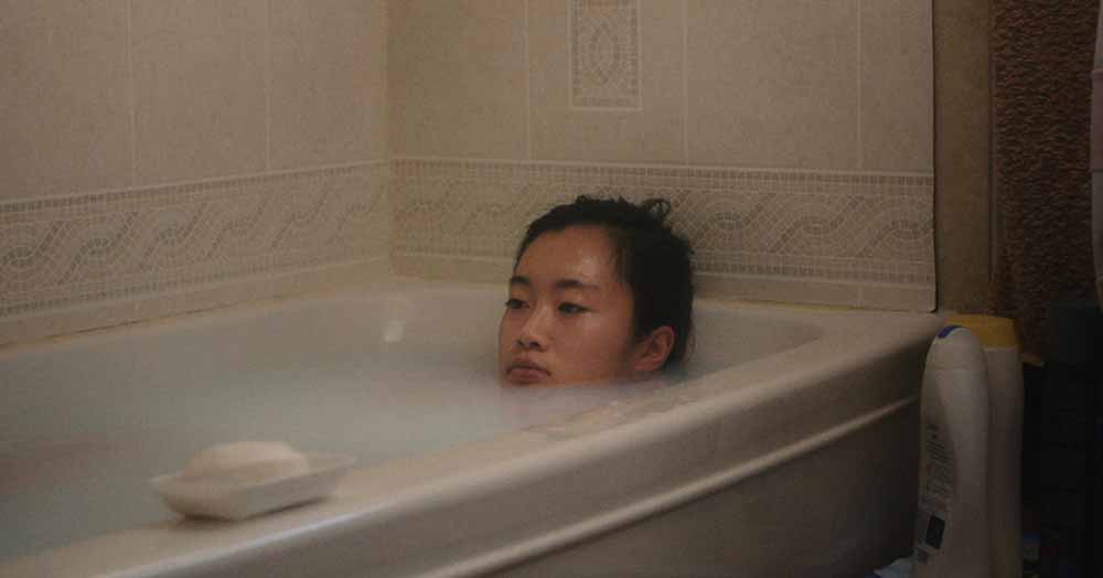 A young woman lies down in a soap filled bath in No Crying at the Dinner Table, one of the best films of the 2020.