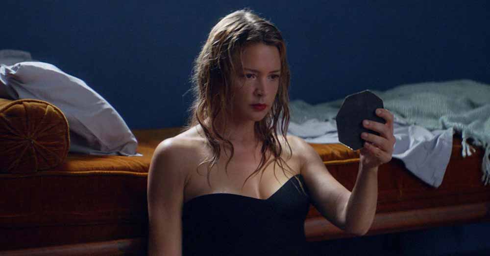 A woman in a fitted black dress stares into a hand mirror in Sibyl, one of the best films of 2020.