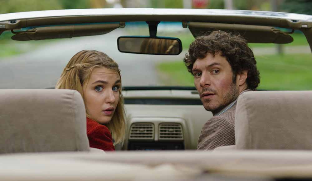 A young girl and a man in his thirties sit in the driver's and passenger's seat of a car, looking behind them toward the backseat, in The Kid Detective.