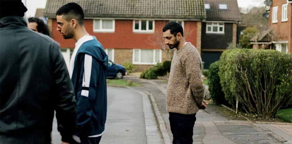 Riz Ahmed stands, head down, outside a suburban home in The Long Goodbye.