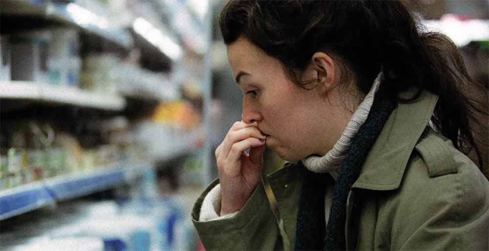 A woman looks at the supermarket shelves, worried, in The Shift, an LSFF 2021 title.