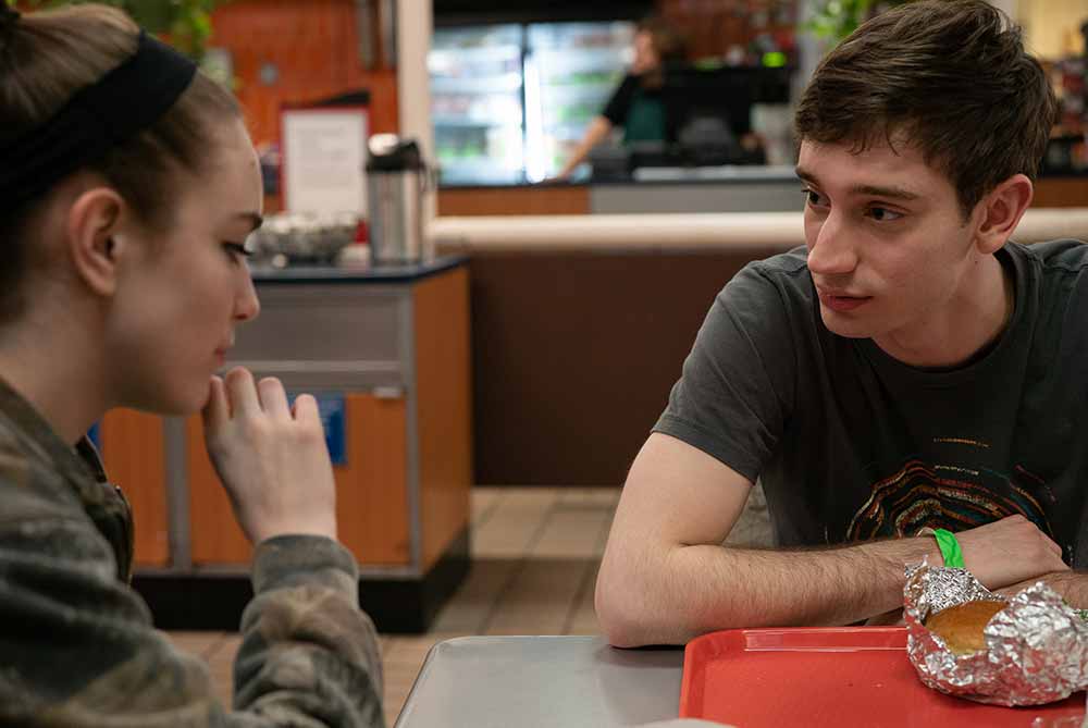 A young woman and a young man, Théodore Pellerin, sit at a diner table on opposite ends of the frame, in conversation, in Never Rarely Sometimes Always.
