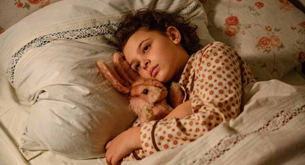 A girl lies in bed with a pink rabbit toy in When Hitler Stole Pink Rabbit.