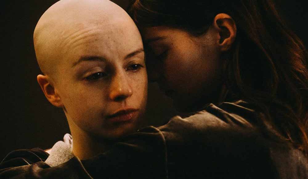 A woman with a shaved head is embraced by another woman in this still from White Lie.