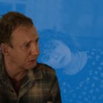 A still of David Thewlis in I'm Thinking of Ending Things, in front of a blue background.