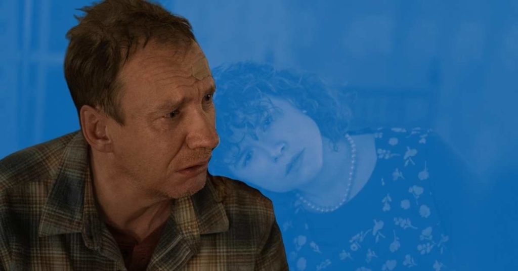 A still of David Thewlis in I'm Thinking of Ending Things, in front of a blue background.