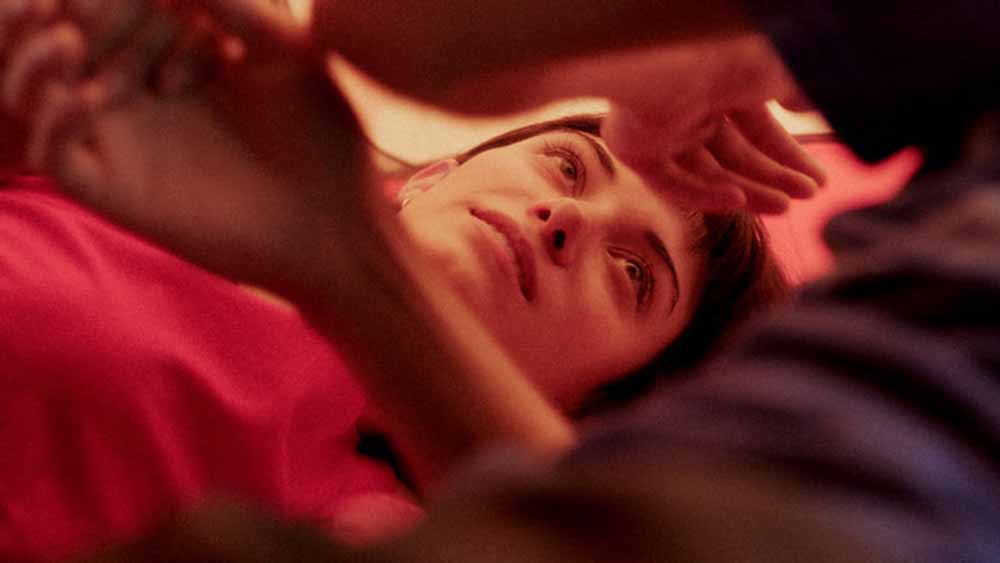 A young woman lies down in a pink hued tent in Friends and Strangers, one of the best films of IFFR 2021.