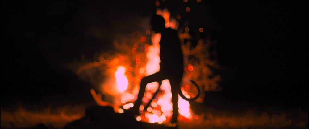 A blurry still of a devil figure silhouetted against a campfire in Identifying Features.
