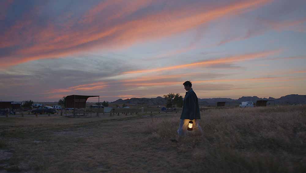 Frances McDormand crosses a vast landscape at magic hour in Nomadland.