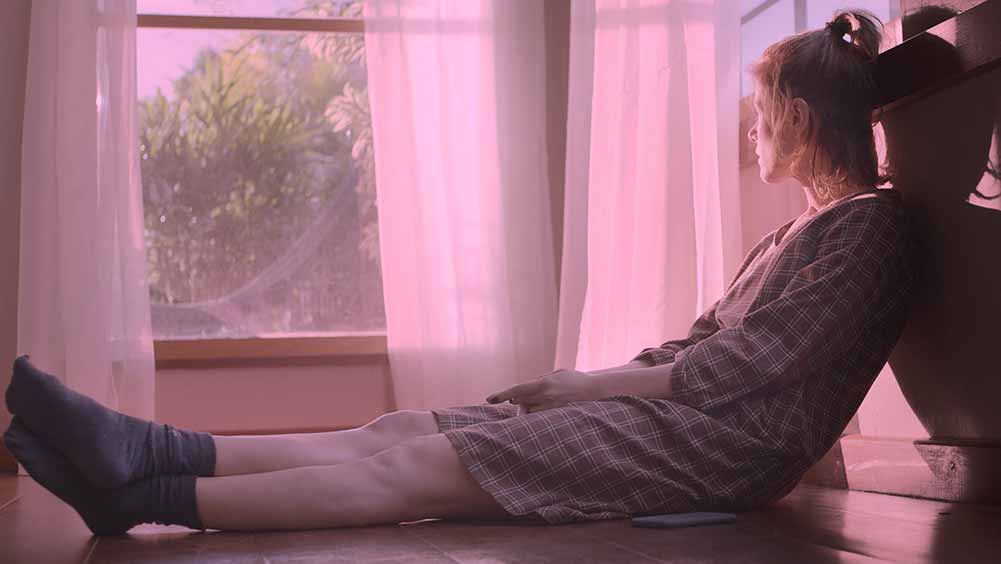 A woman sits looking out of her pink hued window in The Pink Cloud, one of the best films of Sundance 2021.