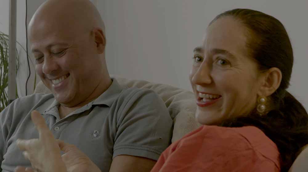 A man and a woman laugh on a sofa together in Miguel's War.