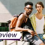 Two young men stand together in the summer sun, looking into the camera. The text on the image reads, 'Review'.