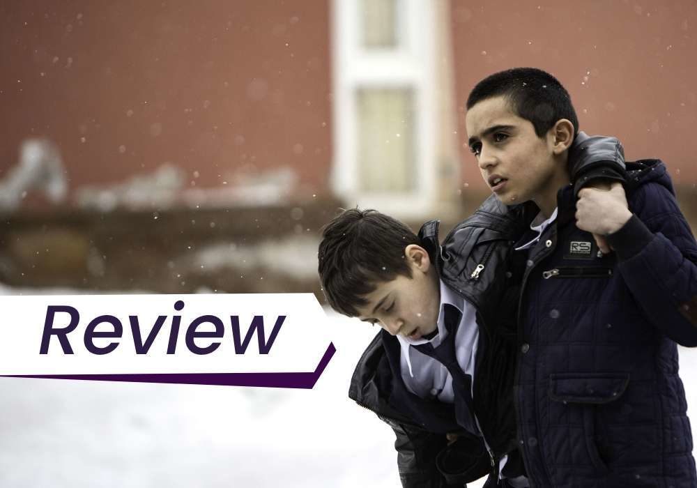A young boy helps carry another young boy through the snow in Brother's Keeper. The text on the image reads, 'Review'.