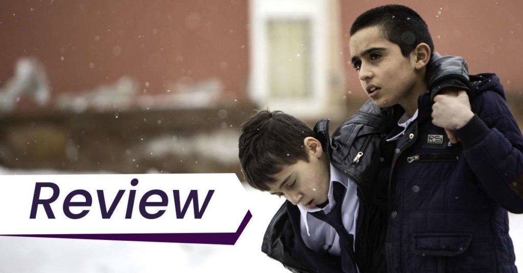 A young boy helps carry another young boy through the snow in Brother's Keeper. The text on the image reads, 'Review'.