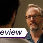 A closeup of an older man, Michael, looking at a man who is almost out of frame in Sublet. The text on the image reads, 'Review'.